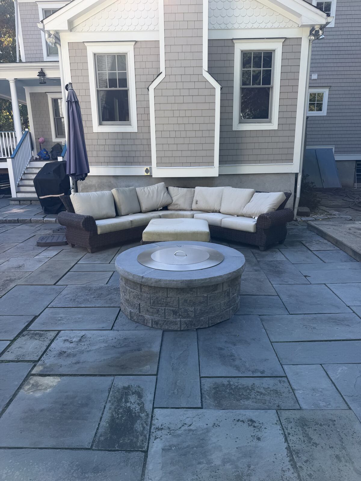Round stone fire feature with a fitted lid and curved wicker seating on a paved patio