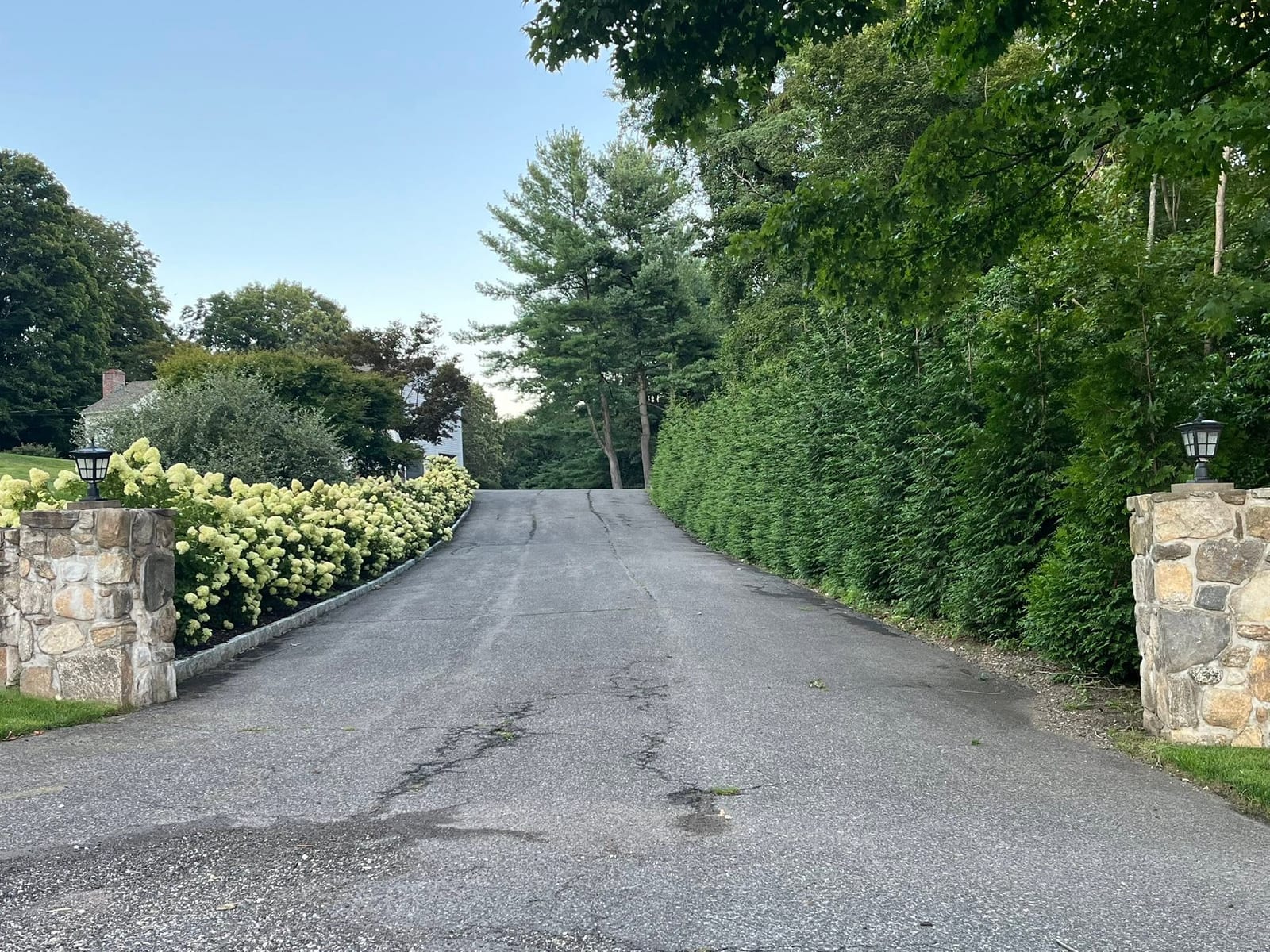 Driveway entrance framed by stone pillars and trimmed hedges